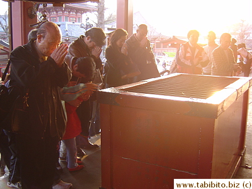 People toss coins into the big red box before praying for their wishes
