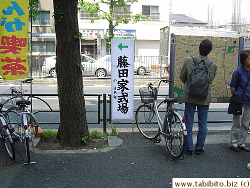 This white sign with black characters at the entrance of a station gives funeral attendants direction and the name of the temple at which the funeral is held