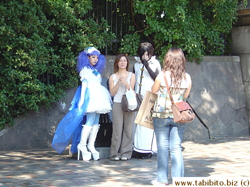 A couple of Cosplay girls' pictures were being taken with a curious stranger. Notice the woman with the black hair even made a cool pose for the photographer