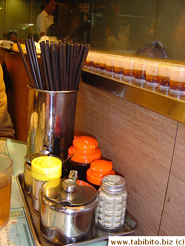 Typical tray of condiments and chopsticks on the tables of a diner.  The single-size servings of chili oil on the window sill are not just for decoration